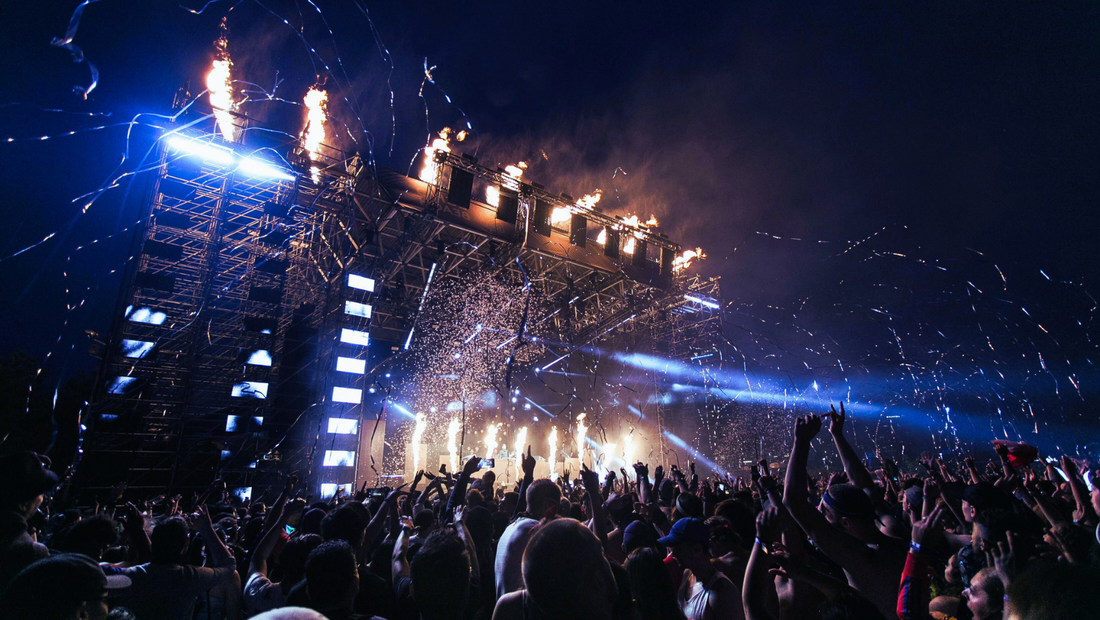 festival stage with lights and firework. Crowd at the front.